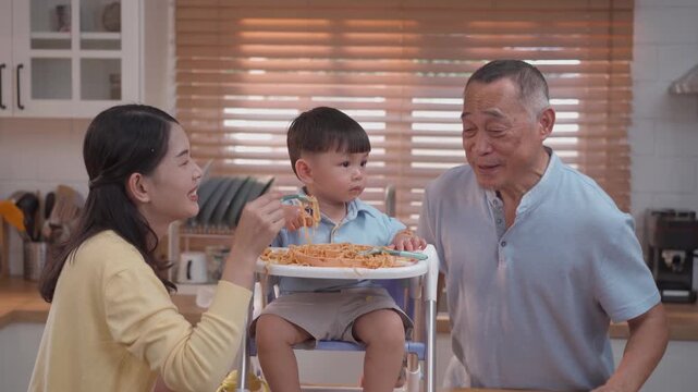Cute toddler playing with spaghetti during mealtime, happy parents encouraging self feeding, messy eating learning, family lifestyle and child development concept