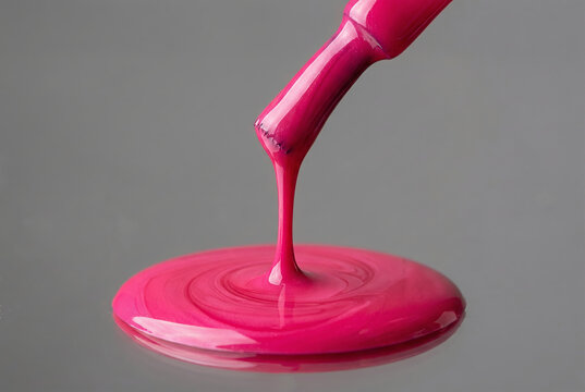 Glossy pink nail polish dripping from applicator brush. Liquid cosmetic texture flowing on smooth surface. Macro shot of vibrant makeup product for beauty salon and fashion skincare style.