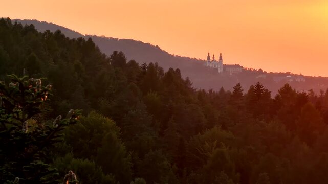 Aerial golden hour view of Kalwaria Zebrzydowska monastery seen through pine branch with cones moving across frame revealing architecture in background