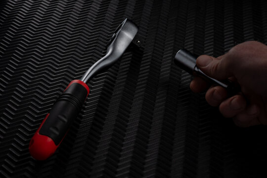 Hand holding socket preparing to attach ratchet wrench on dark textured background
