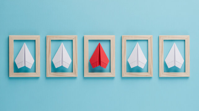 Red Paper Airplane Standing Out Among White Paper Airplanes in Wooden Frames Keywords: paper airplane, red, white, standing out, individuality, leadership, difference