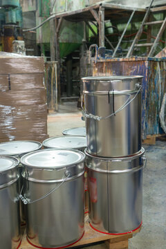 Chemical storage in a manufacturing plant with signs of recent use and logistical preparation. Sealed paint containers and stacked boxes in a production facility interior
