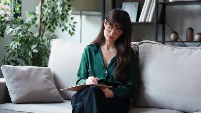 Video of female psychologist taking notes while sitting on the couch in her consultation
