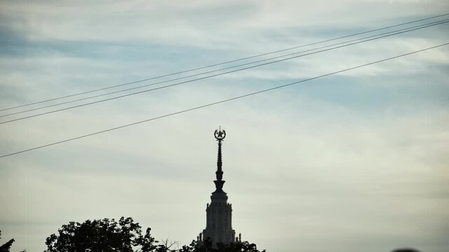 Person ziplining over Moscow State University building against a cloudy sky