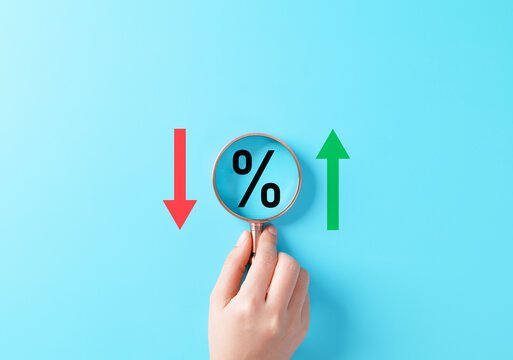 Interest rate increase and decrease concept. Magnifying glass over percentage symbol between red down and green up arrows representing finance analysis, rate change, inflation, loan cost, market trend