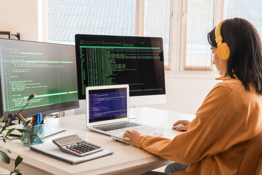 Female programmer with headphones working at desk in office, back view