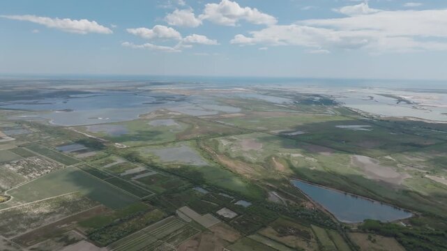 Aerial view of vast Camargue coastal wetland with large shallow lagoons green marsh patches agricultural fields and distant sea under blue sky