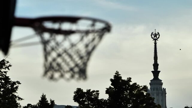 Basketball hoop framing Moscow State University main building spire against sky