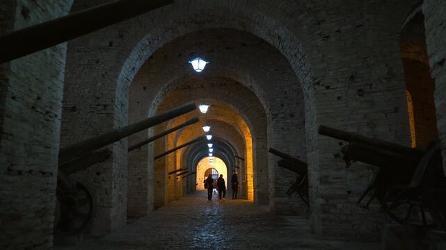 Gjirokaster, Albania - 14th april, 2026: A group of tourists, family with a child, walking down along, dimly lit stone-arched artillery gallery inside historic Gjirokastra Castle, Albania