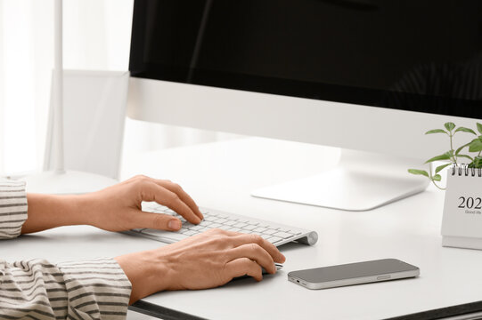 Young female programmer with computer and mobile phone typing on keyboard in office, closeup
