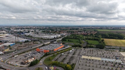 Obraz premium Urban Sprawl Overcast: An aerial view shows a vast expanse of urban development under a cloudy sky, featuring buildings, roads, and parking lots spreading towards the horizon.