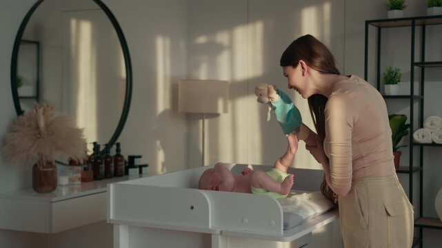 Mother entertains infant with puppet on changing station in softly lit nursery room