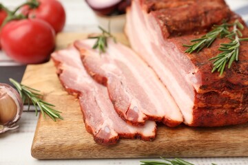 Fototapeta premium Pieces of smoked bacon, garlic, tomatoes and rosemary on light grey wooden table, closeup