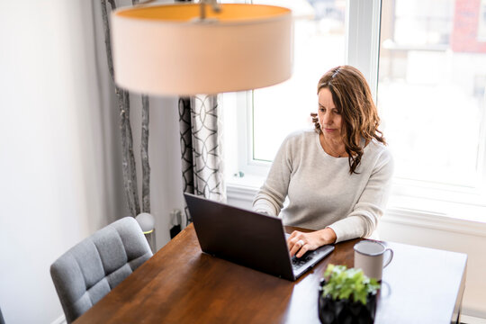 Senior woman at home kitchen table feeling stressed and confused while looking at multiple bills working on her laptop