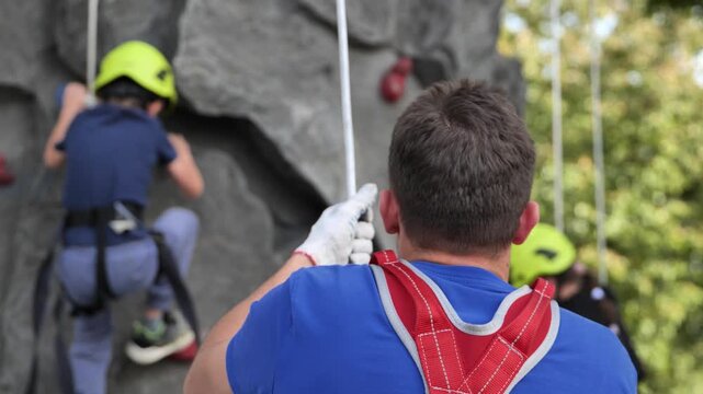 Instructor belaying child during rock climbing activity, ensuring safety and support