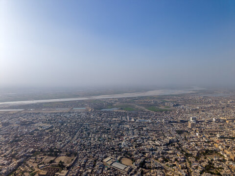 Aerial view of the dense urban landscape and residential buildings near the Indus River under a hazy sky in Hyderabad, Sindh, Pakistan.