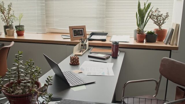 No people shot of workspace with desk with laptop and cluttered with office supplies near windowsill in office