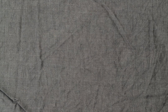 Fabric texture shows creases and folds in gray color, with natural light creating shadows in a simple setting