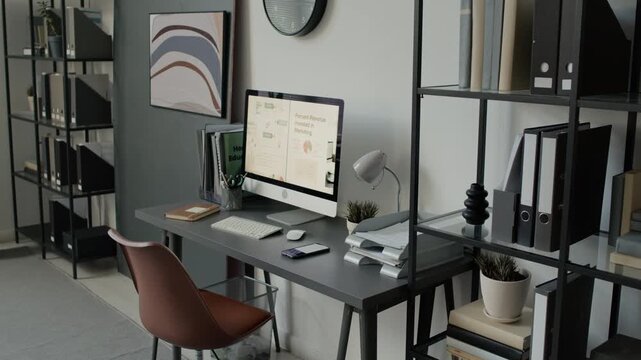 High angle no people shot of modern office workspace with desk, computer, documents, office chair, and shelves holding folders and books