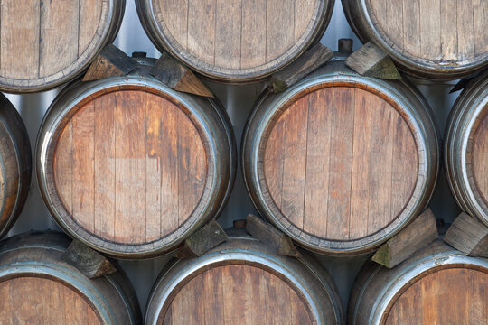 Rows of wooden barrels stacked in a cellar seen during daylight hours in a winery setting