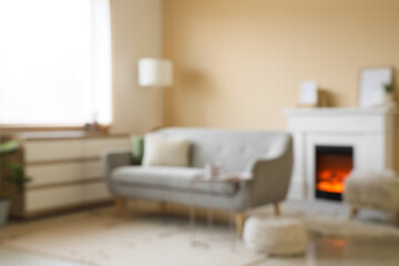 Obraz premium Blurred view of living room with grey sofa, commode and fireplace