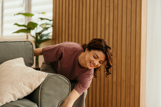 Smiling woman reaching behind sofa finding lost item