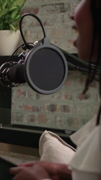 Vertical video: Turning seated woman in white top leaning into mic in studio recording, copy space