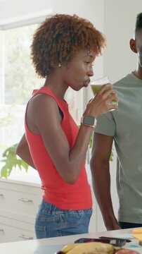 Vertical video: Raising cup, sipping, Black woman testing green juice in kitchen, red top