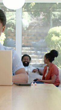 Vertical video: Typing woman in blue top at home table using laptop, phone causing joy, copy space