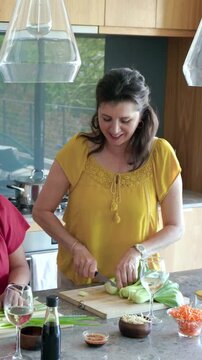 Vertical video: Grabbing knife yellow-blouse woman slicing bokchoy at kitchen island preparing meal
