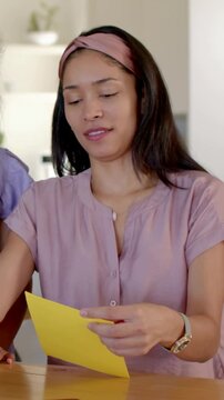 Vertical video: Turning mom in mauve sharing yellow card for mom as daughter leaning in at home
