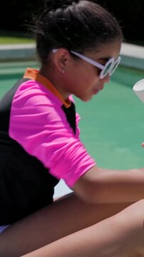 Vertical video: Reaching mom applying sunscreen on daughter poolside for sun care, pink rash guard