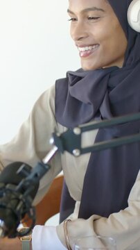 Vertical video: Audio starting host dark hijab headphones podcast mic recording reaching for glass