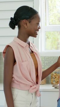 Vertical video: Mom handing tulips and card, teen in tied top hugging family in kitchen, copy space