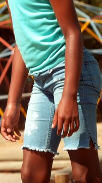 Vertical video: Shifting weight, girl stepping to cross low wooden beam at park, wearing teal tank