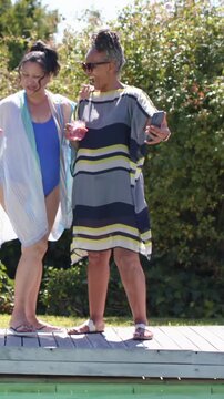 Vertical video: Raising phone, striped dress woman posing for selfie on pool deck holding pink cups