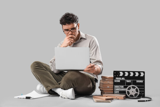 Thoughtful male screenwriter with laptop writing scenario on grey background