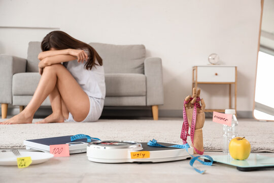 Weight scales with tape measure and food against upset woman at home. Anorexia concept