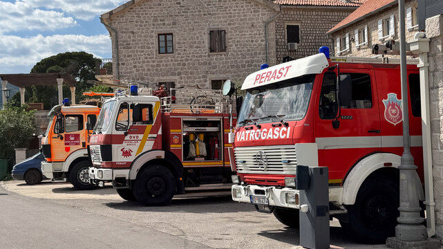  18.04.2026,Perast,Montenegro.Three red fire trucks lined up on a sunny street in a stone-built town, with clear sky and traditional architecture in the background