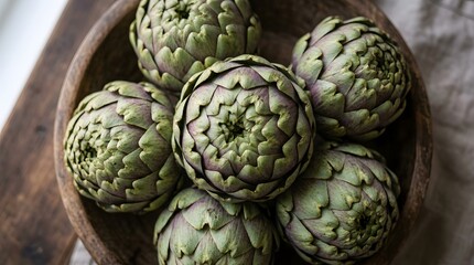 Fototapeta premium Fresh raw artichoke heads lying in a wooden bowl. Organic vegetable harvest for healthy cooking and culinary preparation. Natural ingredients for vegan diet and nutritious food concepts.
