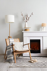 Obraz premium Fireplace, wicker armchair and vase with cotton flowers near white wall in interior of living room