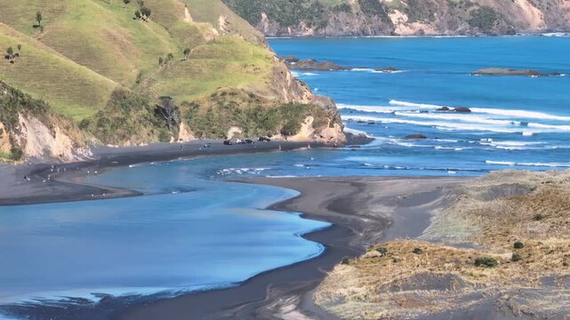 People enjoy a sunny day at Marokopa, Waikato, New Zealand. The black sand beach and rugged coastline offer a picturesque setting for recreation and relaxation.