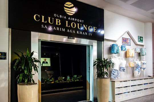 Entrance to the Olbia Airport Club Lounge S.A. Karim Aga Khan IV in Sardinia, Italy, located next to an MC2 Saint Barth clothing retail display.