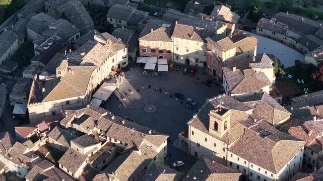 Aerial view of the circular Piazza del Comune surrounded by historic stone buildings and terracotta rooftops in Montefalco, Umbria, Italy.