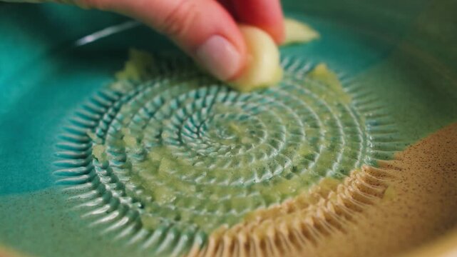 Hand grating fresh garlic on ceramic garlic grater plate, traditional Spanish ajo rallador or plato rallador. High quality 4k footage