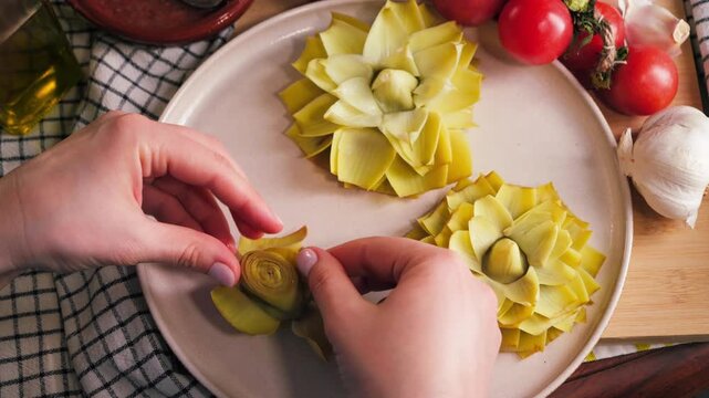 Close up of hands opening cooked artichoke petals to prepare Spanish dish Flores de alcachofa, traditional cuisine concept. High quality 4k footage