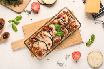 Naklejka premium Baking dish with eggplant slices, ground meat, vegetables and cheese on light background