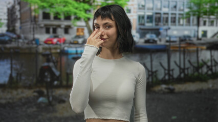 Fototapeta premium Young hispanic woman pointing finger at camera on street in amsterdam with direct gaze; vigilance alertness.