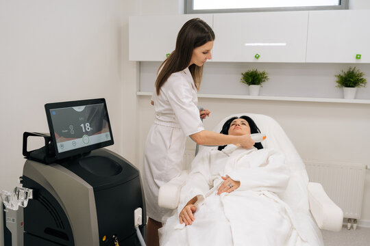 Relaxed middle-aged woman receiving modern hardware cosmetology procedure for facial skin rejuvenation from beautician, non invasive treatment for antiaging and skin tightening in beauty salon.