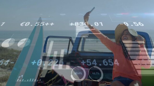 Woman on truck bed raising phone taking selfie at beach activating travel HUD charts over surfboard